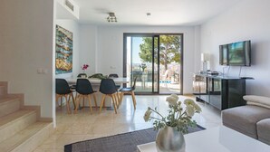 A modern living room with a sofa, a flat-screen TV, and a dining area with chairs and a table.