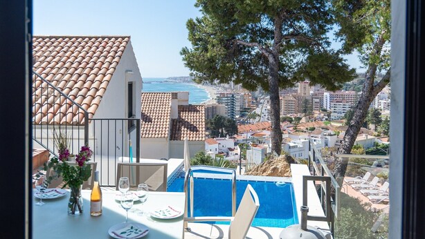 A balcony with a table set for dining, a pool, and a view of the cityscape.