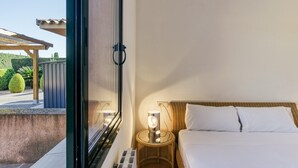 Ein Schlafzimmer mit einem Bett, einem Nachttisch mit Lampe, einem Fenster und Blick auf einen Garten.