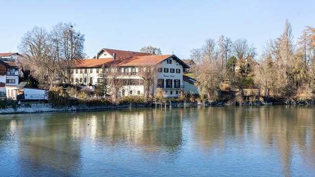 A riverside building with a red roof, white walls, and a sign that reads 'Hotel Post.'