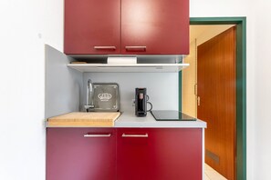 A compact kitchenette with a coffee maker, a toaster, and a cutting board on the countertop.