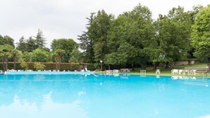 Ein Schwimmbecken mit Liegestühlen und einer Laube in einer parkähnlichen Umgebung.