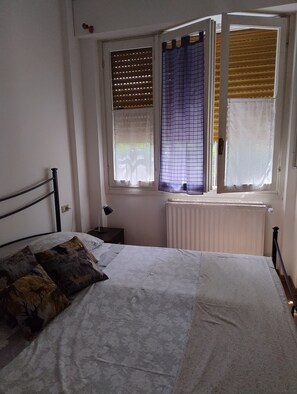 Una camera da letto con un letto, un comodino, una lampada e una finestra con persiane.