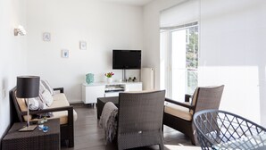 Una sala de estar moderna con un sofá, una mesa de comedor, un televisor y un ventanal grande.