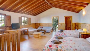 Una habitación acogedora con vigas de madera, una cama con ropa de cama floral, un sofá, un televisor y un escritorio de madera.