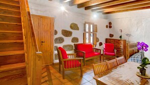 Un interior rústico con una escalera de madera, detalles en pared de piedra y un comedor con mobiliario de madera.