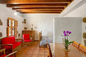 A room with a wooden ceiling, a bed with a checkered bedspread, a red sofa, a wooden chair, a small table with a vase of flowers, and a wooden bench. - Vacation Home Mirador de Domingo with Mountain View, Sea View, Terraces & Garden (Gáldar)