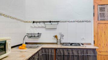 Una cocina con microondas, fregadero y estufa. Hay naranjas en la encimera, una cesta y un colgador con tazas.