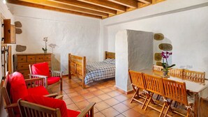 Una habitación con una cama, una silla de madera, una mesa de comedor y un mueble pequeño.