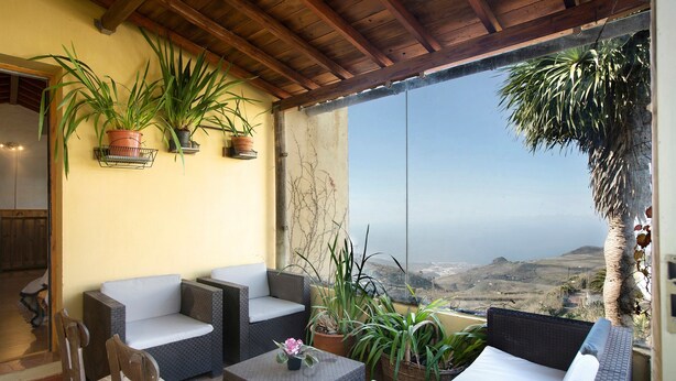 Un balcón con mobiliario de mimbre, plantas en macetas y vistas al paisaje.