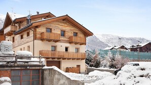 Un bâtiment en bois à plusieurs étages, doté de balcons, d’un mur en pierre et surplombant un paysage montagneux enneigé.