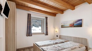 Une chambre avec deux lits, une fenêtre avec des rideaux, un tableau au mur et des poutres en bois au plafond.