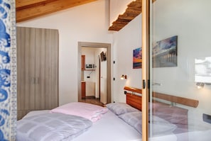 Une chambre à coucher comprenant un lit, une armoire, une porte donnant sur une salle de bain et un tableau accroché au mur.
