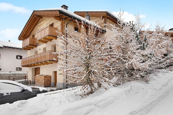 Una cabaña de madera con balcones, un camino cubierto de nieve y una pila de leña.