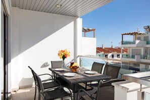 A balcony with a table set for dining, chairs, a vase with flowers, and a view of buildings.