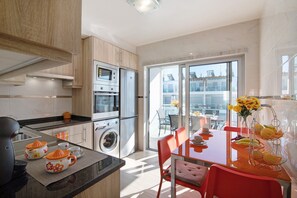 A modern kitchen with built-in appliances, a dining area with a table and chairs, and a view through a glass door.