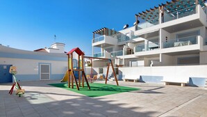 Ein Spielplatz mit Schaukeln, einer Rutsche, einer grünen Matte und einer barrierefreien Spielkonstruktion.