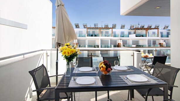 Ein Balkon mit einem Tisch für zwei Personen, einer Vase mit gelben Blumen und einer Obstschale.
