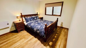 A bedroom with a wooden bed, a nightstand, a lamp, a ceiling fan, and a window with blinds. - Treetops Hideaway*Hikes*Close to Town*Nature (West Albury)