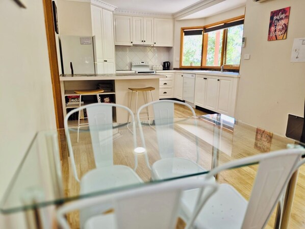 A modern kitchen with white cabinets, a glass dining table, and two bar stools. - Treetops Hideaway*Hikes*Close to Town*Nature (West Albury)