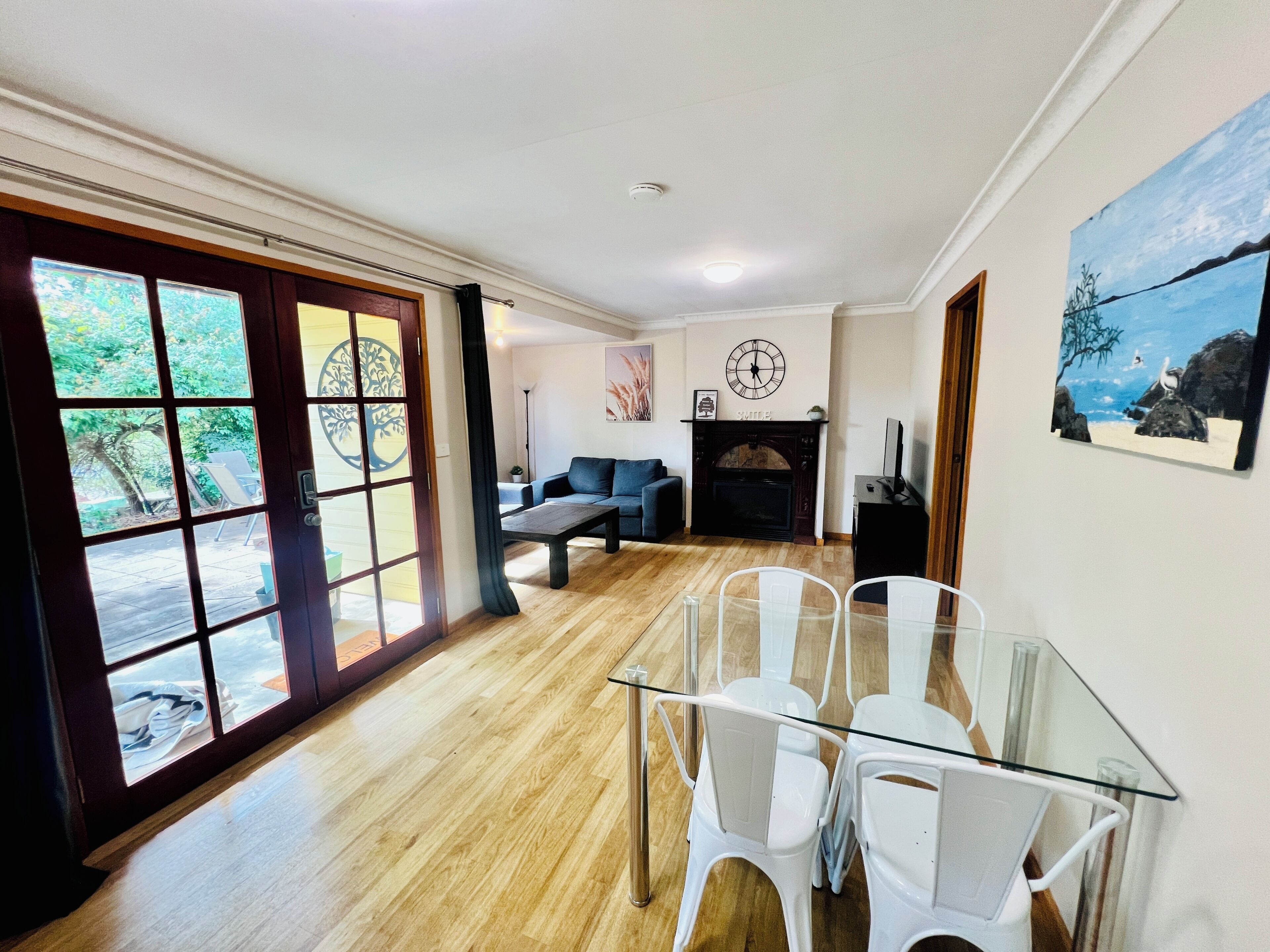 A spacious living area with a fireplace, a dining table with chairs, and a large window with a view of greenery.