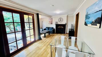 A spacious living area with a fireplace, a dining table with chairs, and a large window with a view of greenery.