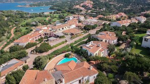 Zona residencial costera con casas de techos de teja anaranjada, una piscina y vistas al mar.