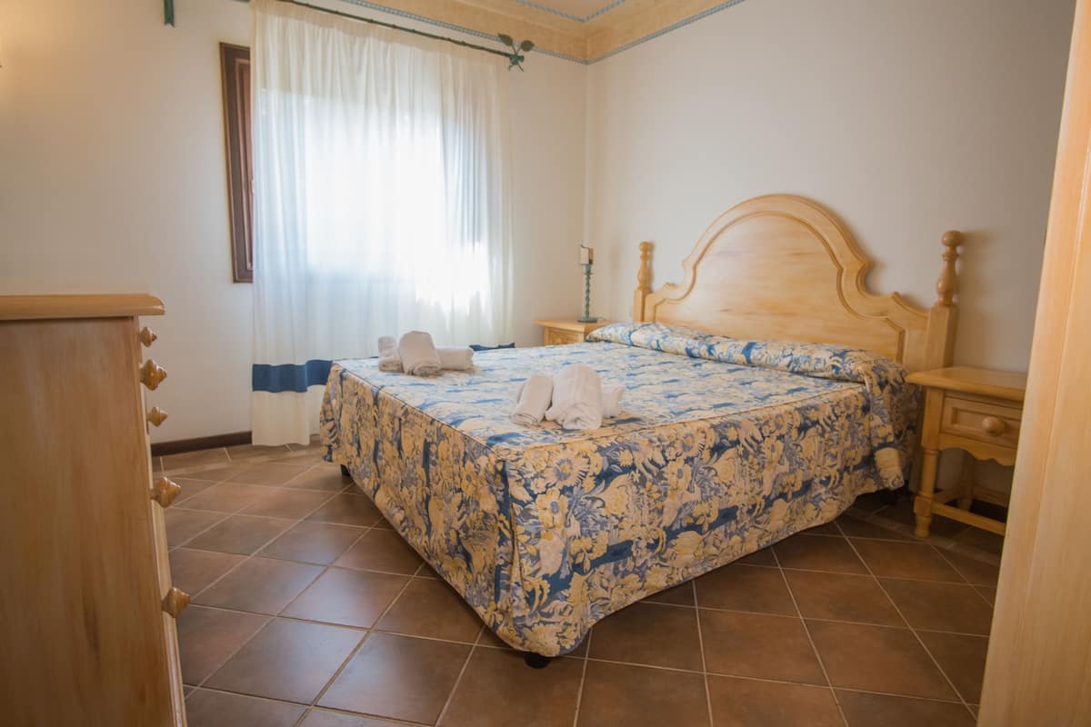 Un dormitorio con cama de madera, una mesita de noche, un aparador y una ventana con cortinas.