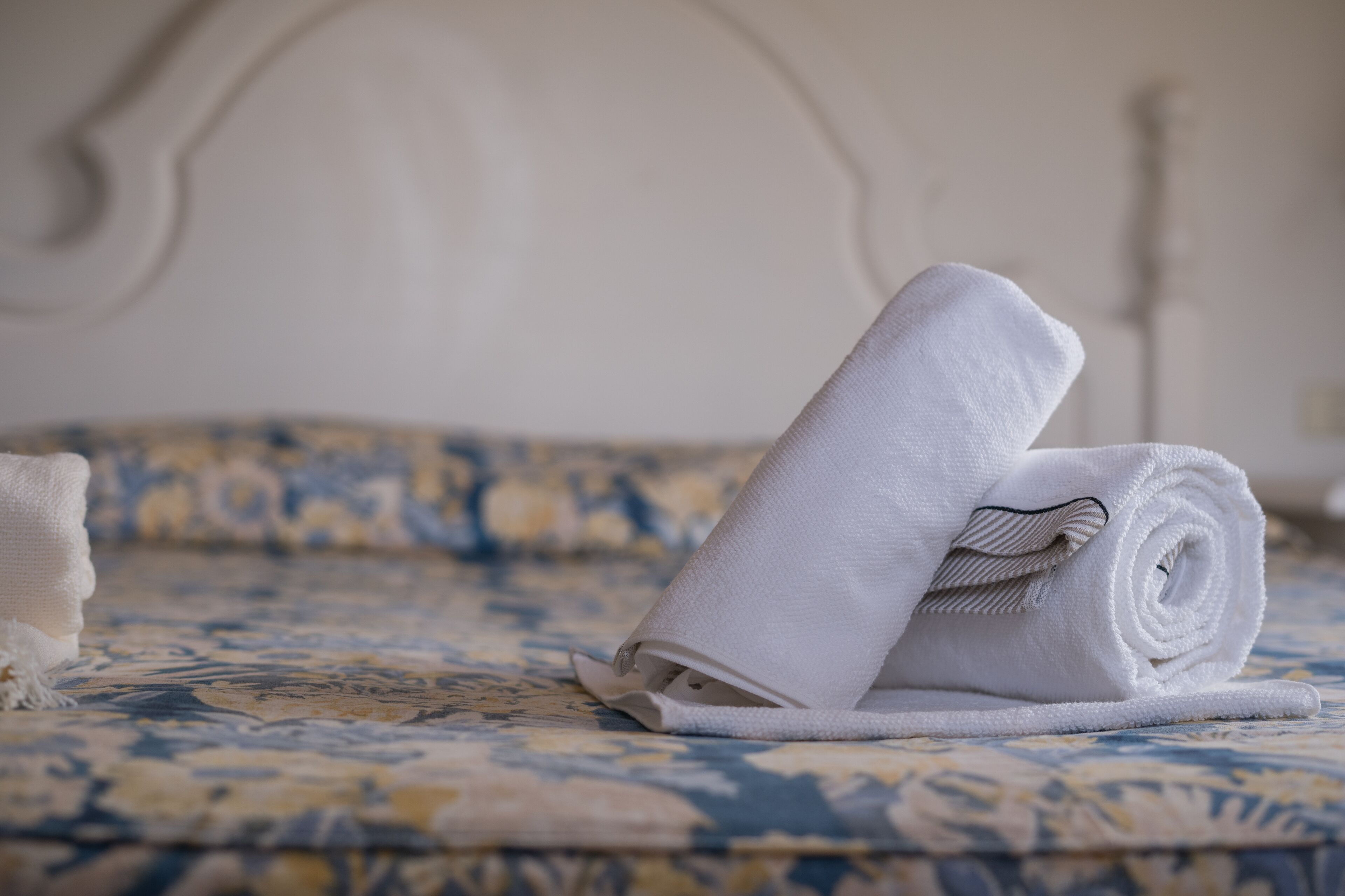 Un lit bien fait, recouvert d’une couvre-lit à motifs et sur lequel est posée une serviette blanche enroulée.
