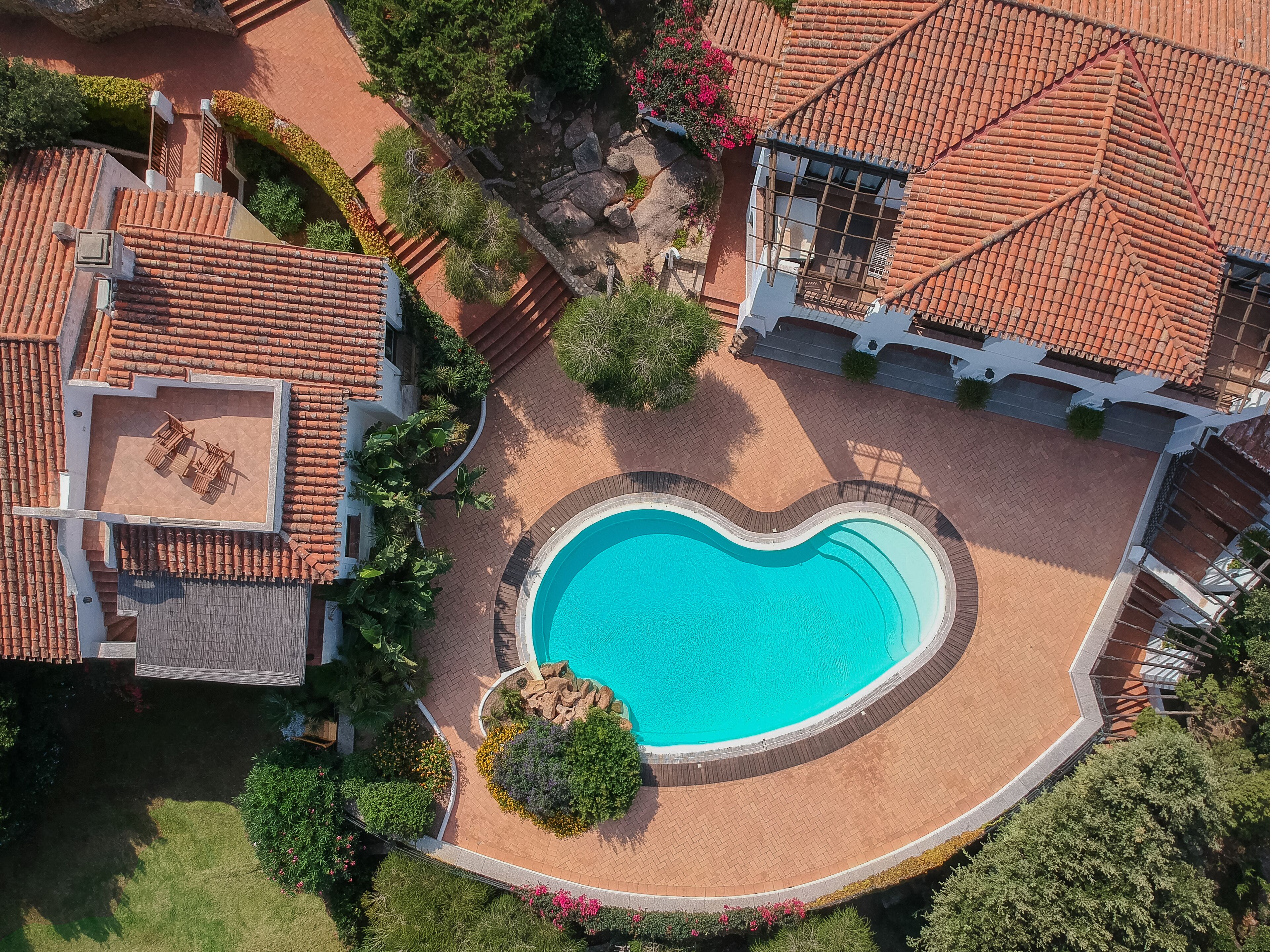 Vista aérea de una propiedad con piscina en forma de corazón, rodeada por un camino de ladrillo y abundante vegetación.