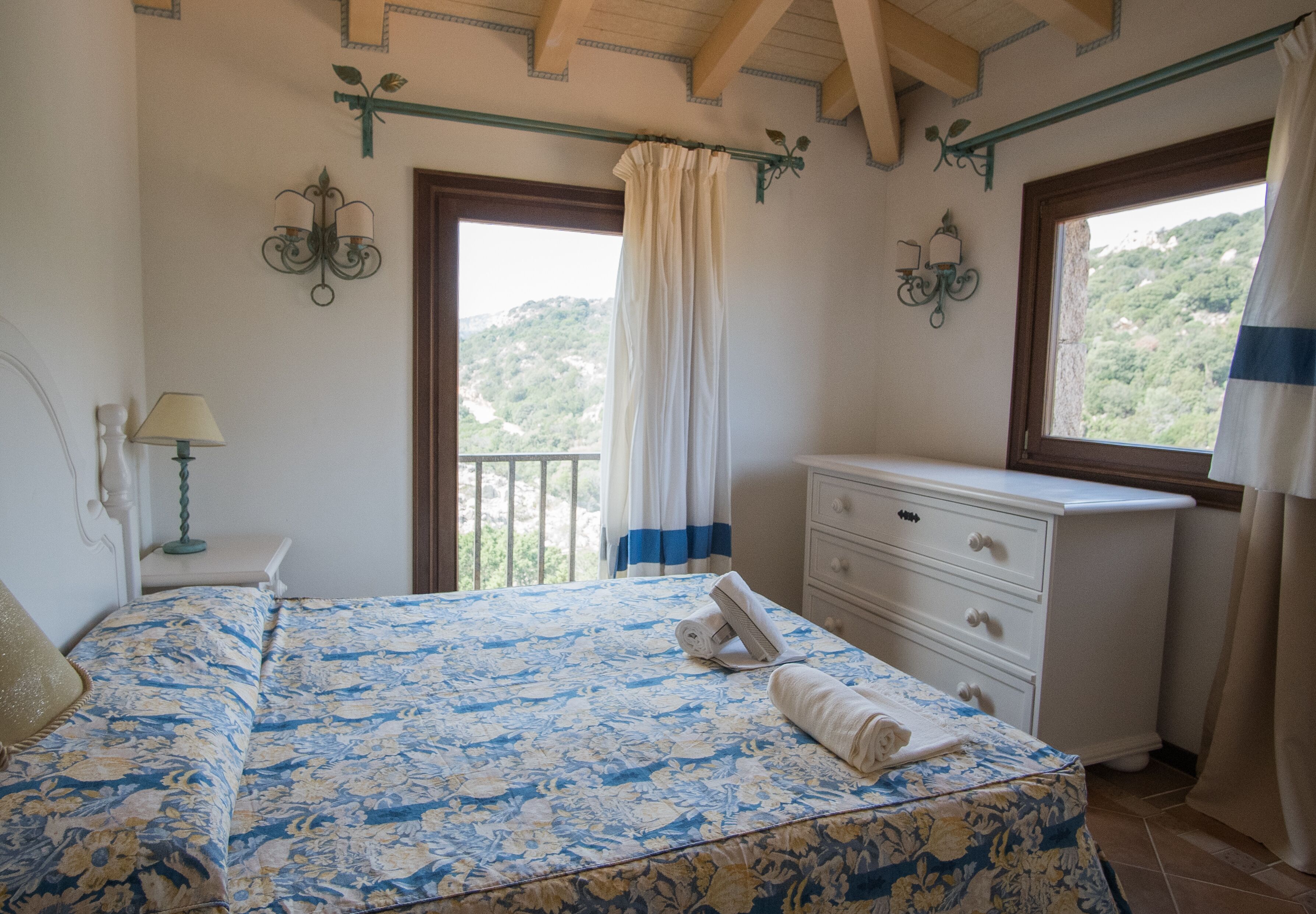 Une chambre à coucher comprenant un lit, une commode, une table de chevet et une fenêtre donnant sur un paysage verdoyant.
