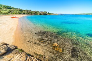 Une plage à l’eau turquoise et limpide, un bateau échoué sur le sable et une côte rocheuse.