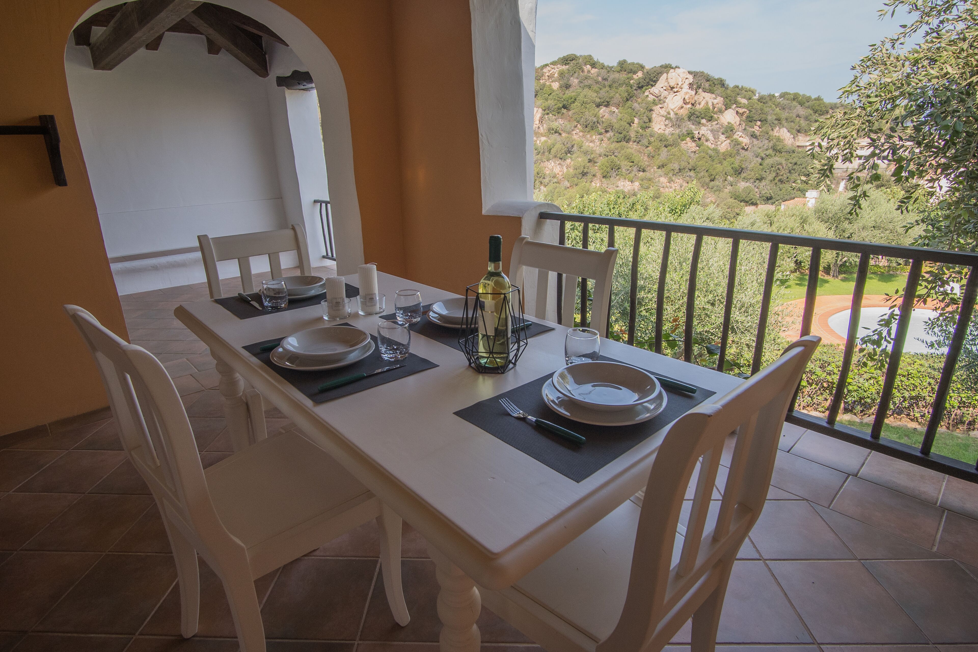 A dining table set with plates, glasses, and a bottle, overlooking a mountainous landscape.