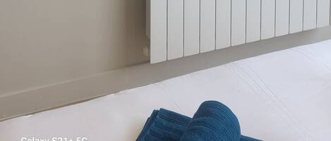 Ein Zimmer mit einem an der Wand befestigten Flachbildfernseher, einem weißen Heizkörper und einem Bett mit blauer Bettwäsche.