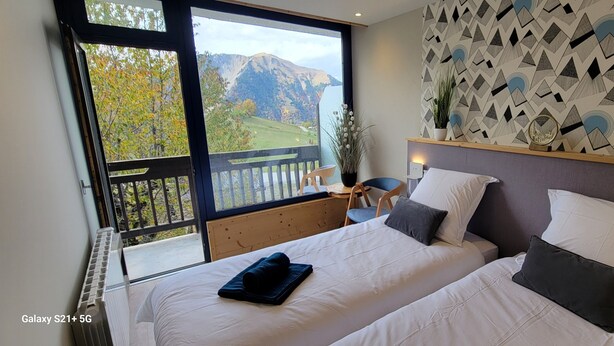 Ein Schlafzimmer mit zwei Betten, einem Balkon mit Bergblick und einer Wand mit geometrischem Muster.