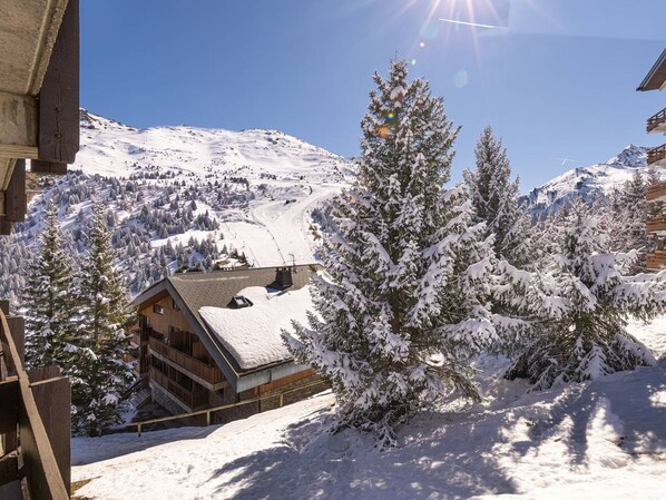 A wooden building with a sloped roof, surrounded by snow-covered trees and a mountainous backdrop.