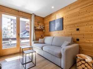 Moderni sisustus, jossa on puuseinä, harmaa sohva, pieni pöytä ja ikkuna, josta avautuu näkymä rakennuksiin.