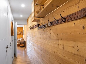 Un couloir aux murs lambrissés, avec un porte-manteau et une porte donnant sur une pièce où se trouvent un canapé et une cheminée.