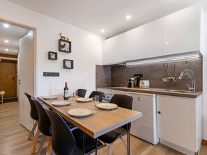 Eine moderne Küche mit weißen Schränken, einem Holztisch, schwarzen Stühlen und einem Einbauofen.