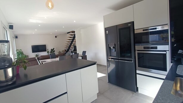 A modern kitchen with a central island, stainless steel appliances, and a staircase leading to another level. - Vacation home rental Gulf of Morbihan (Sarzeau)