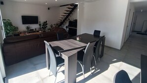 A modern living space with a dining area, a staircase, and a flat-screen TV. - Vacation home rental Gulf of Morbihan (Sarzeau)