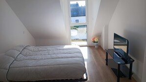 A bedroom with a bed, a small table with a TV, and a window with a view of buildings. - Vacation home rental Gulf of Morbihan (Sarzeau)