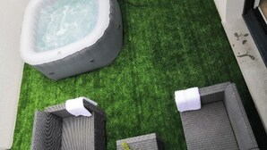 A hot tub on artificial grass, two wicker lounge chairs, and a small table with a flower arrangement. - Vacation home rental Gulf of Morbihan (Sarzeau)