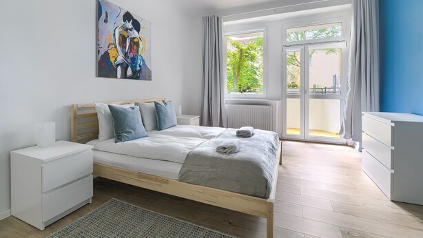 A bedroom with a bed, bedside tables, a dresser, a window with curtains, and a painting on the wall.
