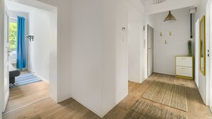 A hallway with a wooden floor, white walls, and a blue curtain in the background. There is a white cabinet with gold handles and a mirror with a gold frame.