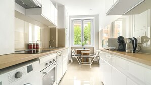 A modern kitchen with white cabinetry, a built-in oven, a washing machine, and a dining area with a table and chairs.