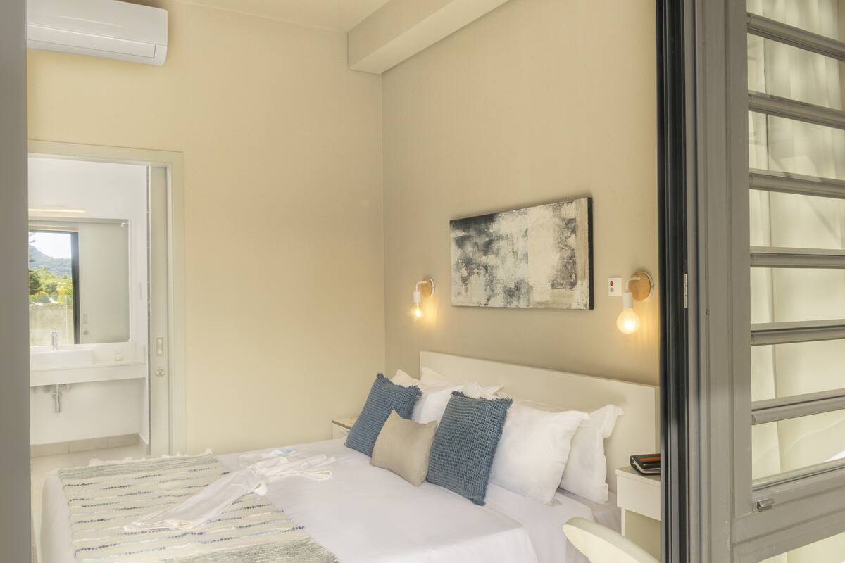 Un dormitorio con cama, ventana, luz instalada en la pared y un cuadro.
