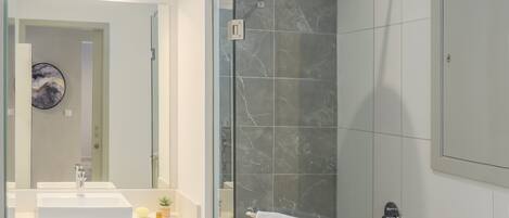 A modern bathroom with a glass-enclosed shower, a white sink, and a marble-tiled shower wall.