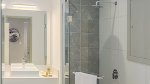 A modern bathroom with a glass-enclosed shower, a white sink, and a marble-tiled shower wall.