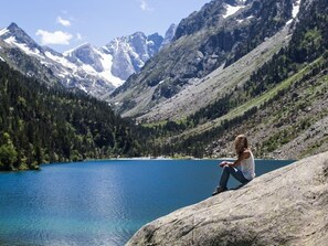 A person sitting on a rock overlooking a clear blue lake with mountains in the background.